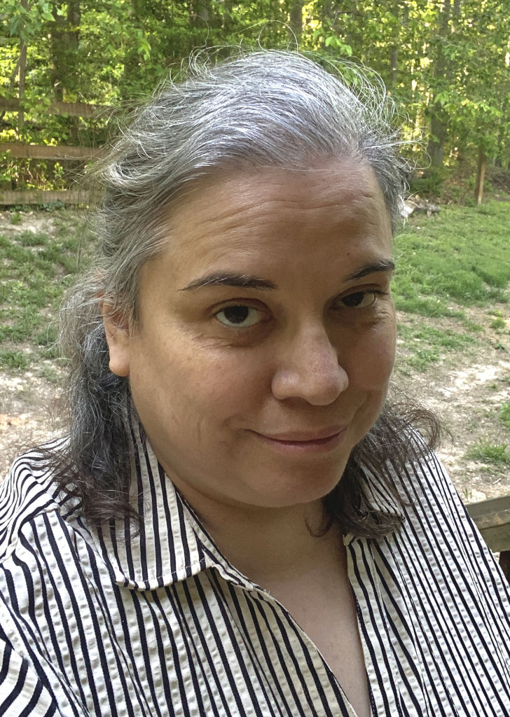 A woman with long dark slightly graying hair smiling.